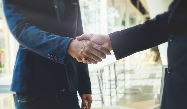 Two businessmen shaking hands inside a corporate office